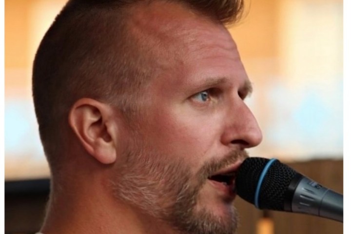 Profile of a person singing into a microphone outdoors.