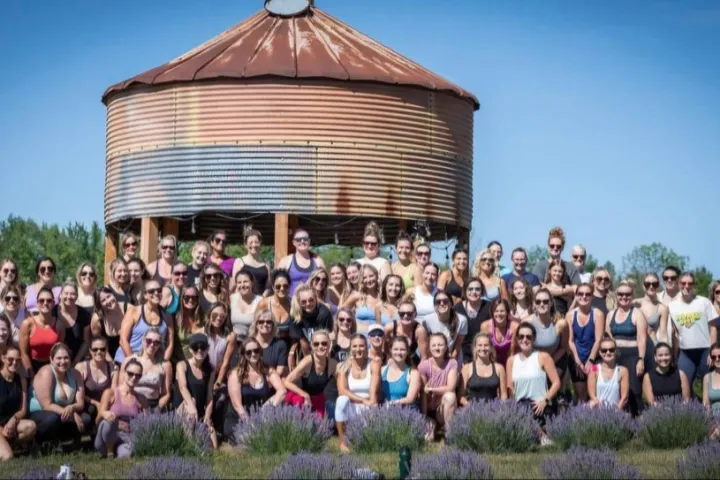 Group of people posing in front of a large rusted silo on a sunny day.
