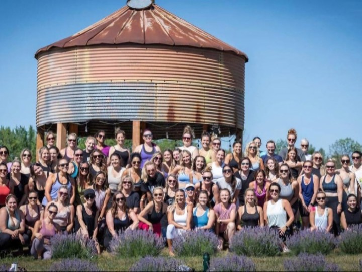 Group of people posing in front of a large rusted silo on a sunny day.
