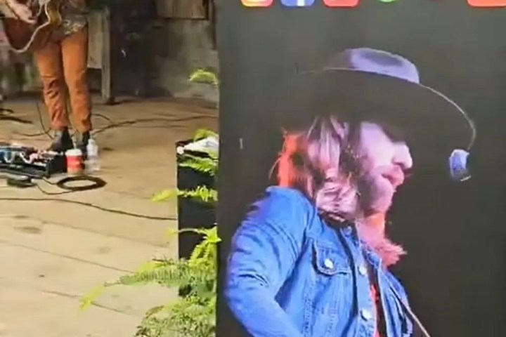 Musician performing with guitar near a promotional banner.