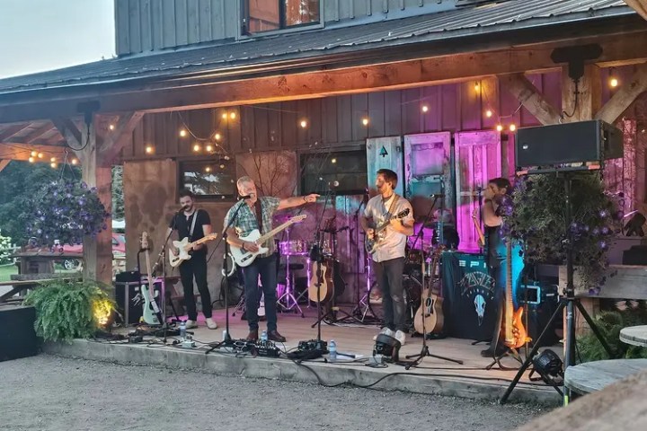 Outdoor band performance under string lights on a wooden stage with a rustic building backdrop.