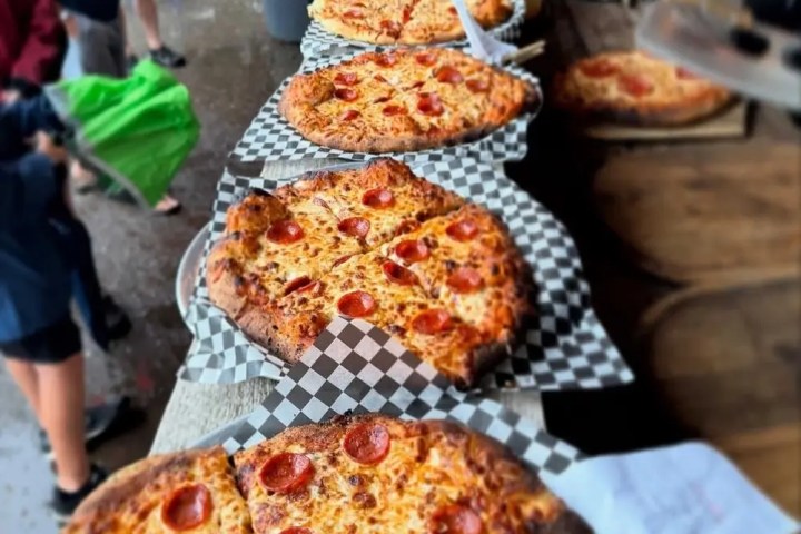Several pizzas with various toppings on a table lined with checkered paper.