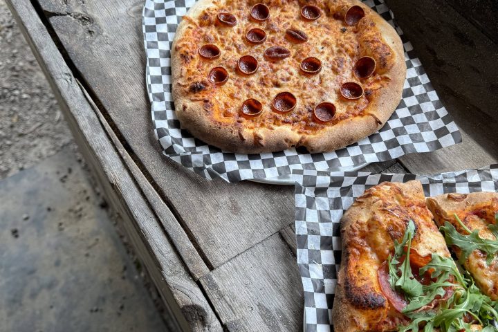 Three pizzas on a wooden surface, each with different toppings, including pepperoni and arugula.