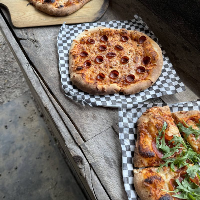 Three pizzas on a wooden surface, each with different toppings, including pepperoni and arugula.
