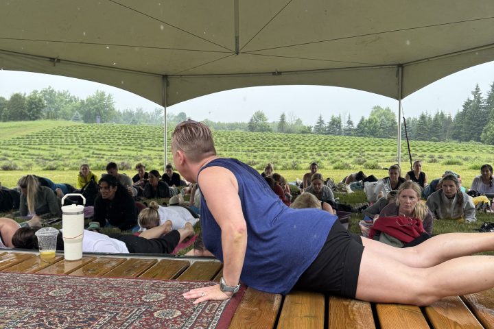 Person doing yoga on a wooden platform under a tent with people watching in a field.