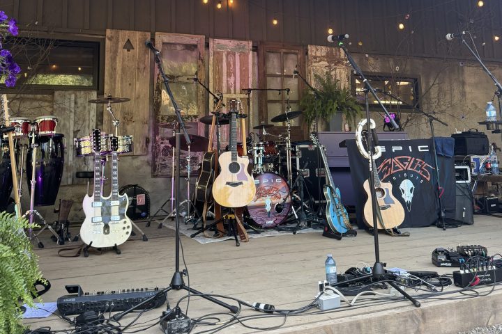 Outdoor stage with guitars, drums, and microphones ready for a band performance under string lights.