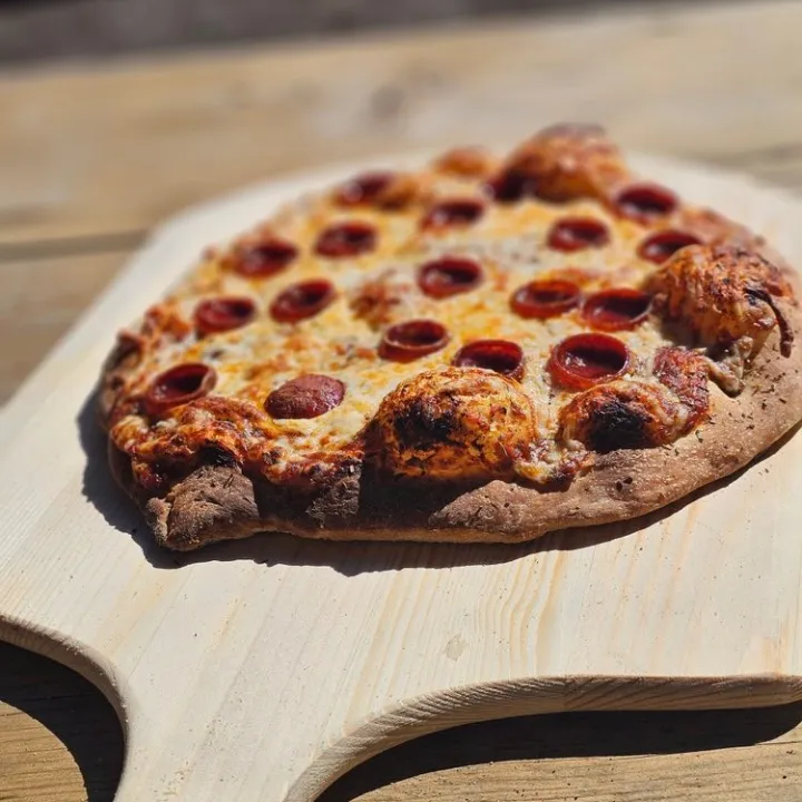 Pepperoni pizza on a wooden pizza peel under sunlight.
