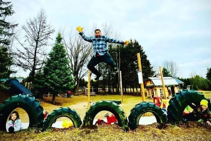Person jumping over large tires with kids playing inside them in a park setting.