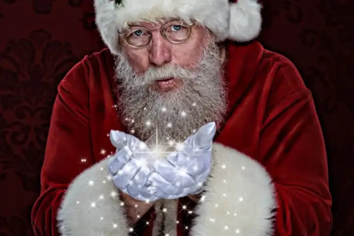 Santa holding glowing light in his hands, wearing red and white suit against dark red background.