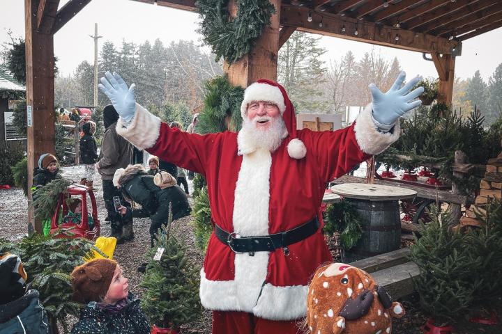 Santa Claus greeting children under a decorated wooden gazebo at an outdoor Christmas market.