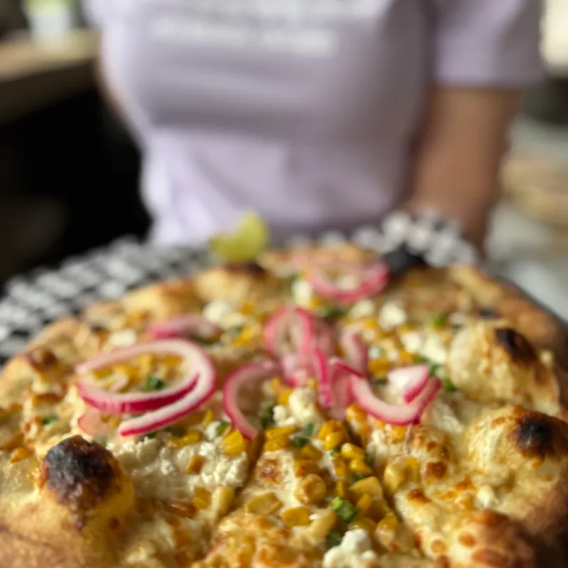 Pizza with corn and pickled onions on a checkered platter.