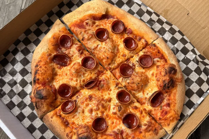 Pepperoni pizza in an open box on a wooden table.