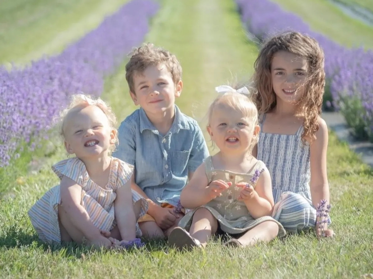 Four children sitting on grass with lavender fields in the background.