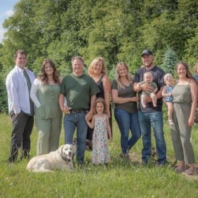 A family with a dog stands in a grassy field with trees in the background.