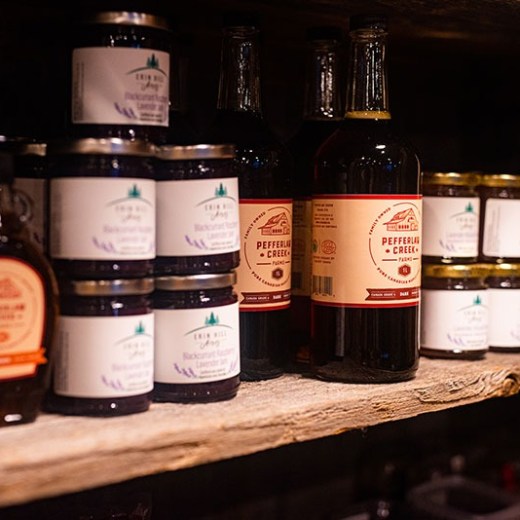 Jars and bottles of jam, syrup, and sauces on a wooden shelf.
