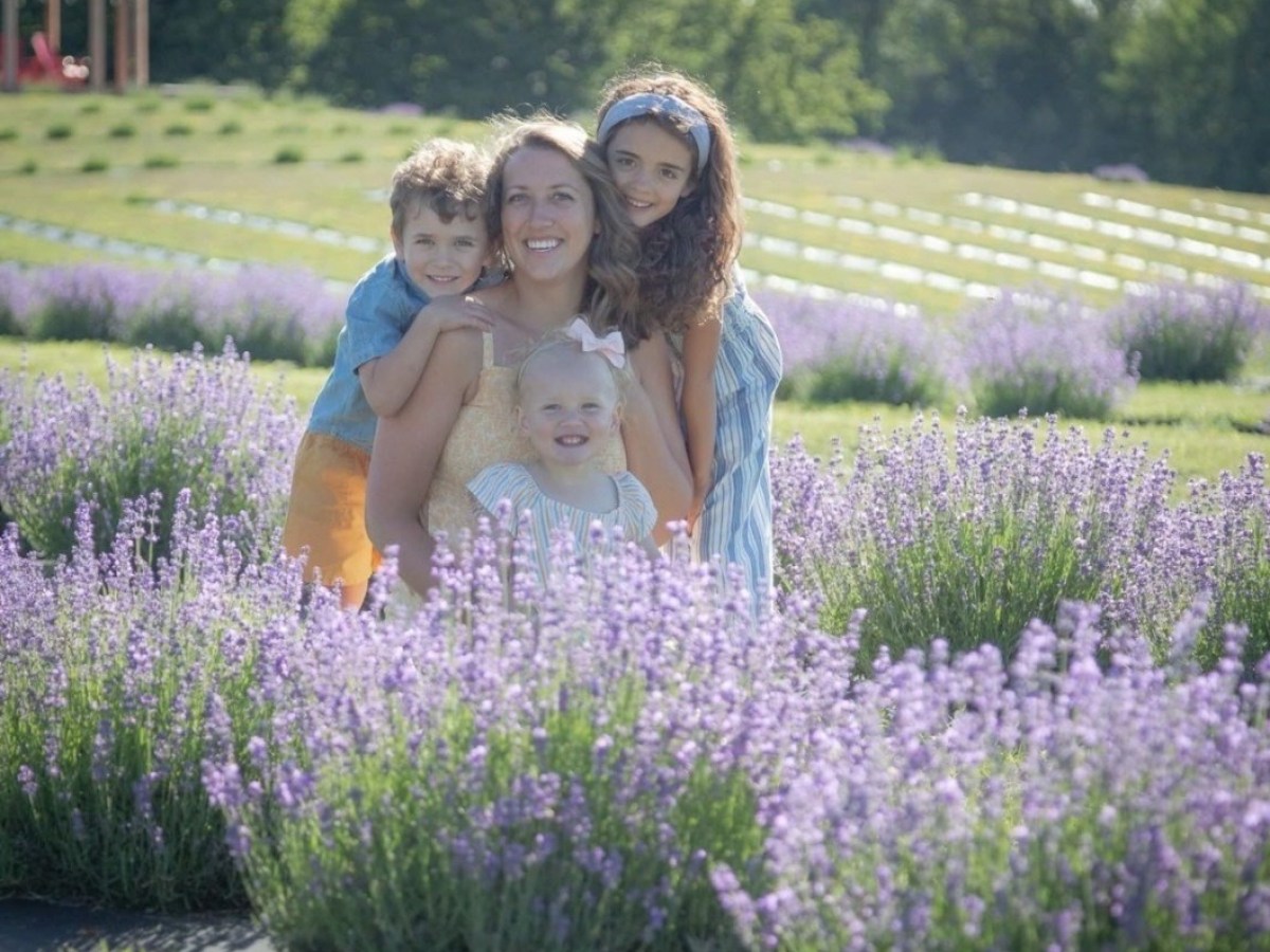 Woman with three children smiling in a lavender field on a sunny day.