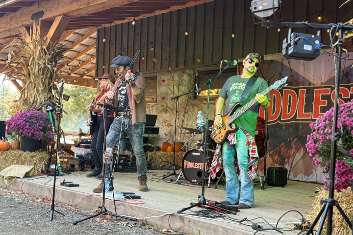 Band performing on a rustic outdoor stage with hay bales and autumn decor.