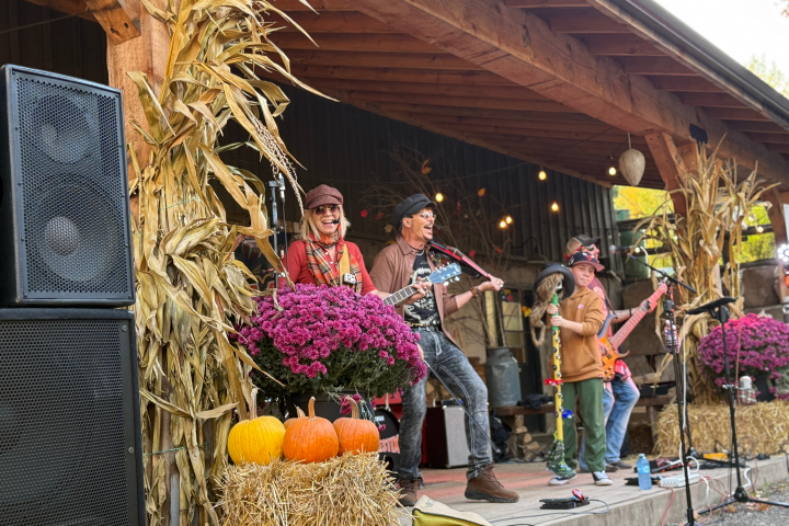 Musicians perform on a festive outdoor stage with hay bales and autumn decor.