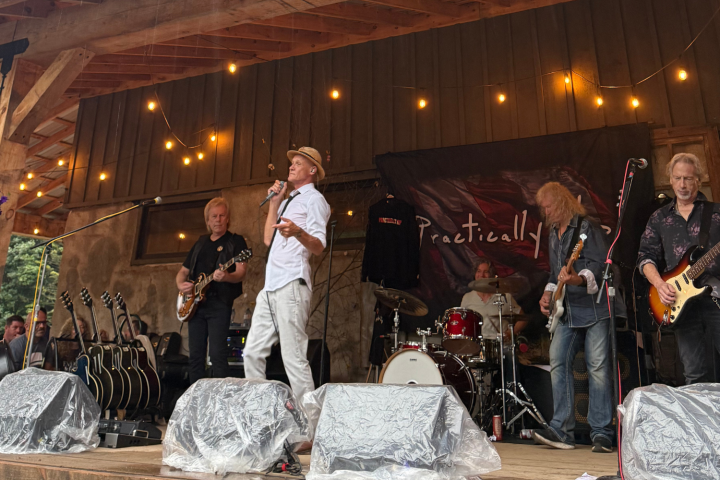 Band performing on a wooden stage with string lights overhead, guitars and drums visible.