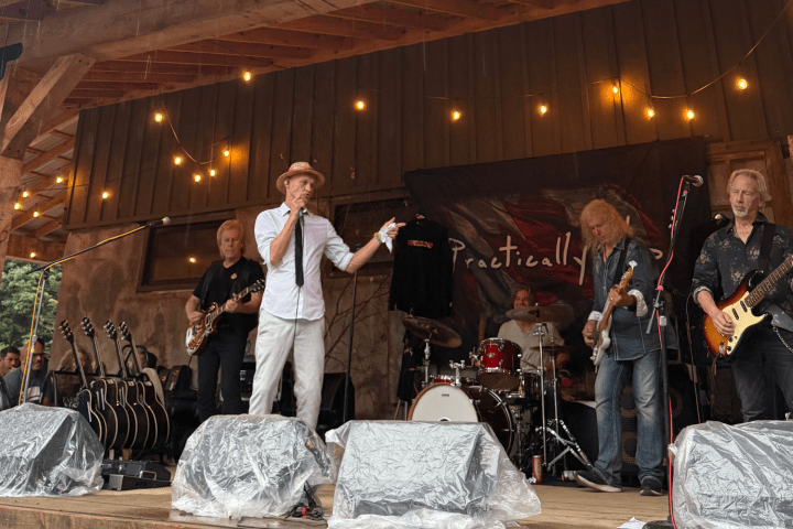 Band performing on a wooden stage with guitars, drums, and vocalist under string lights.