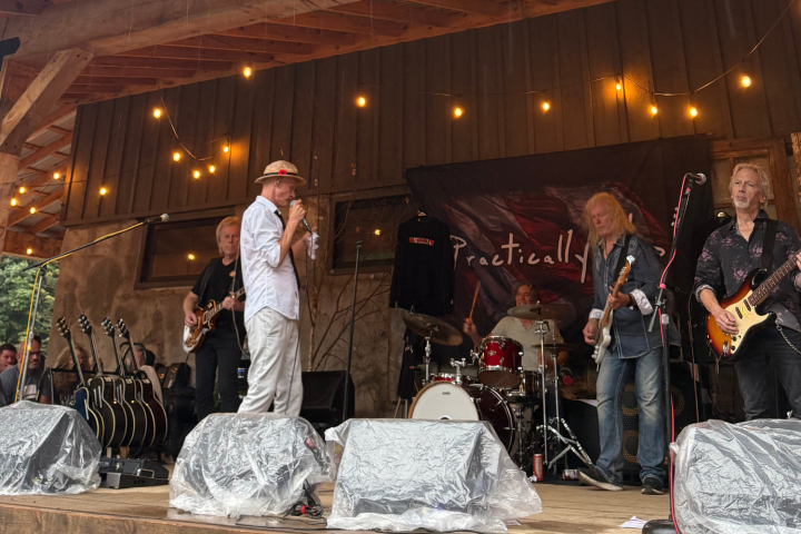 Band performing on outdoor stage with string lights and covered speakers.