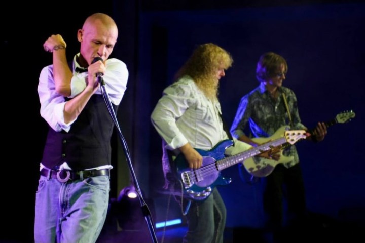 Three musicians performing on stage with guitars and a microphone.