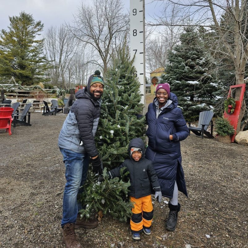 Family posing with a Christmas tree beside a height measurement scale outdoors.