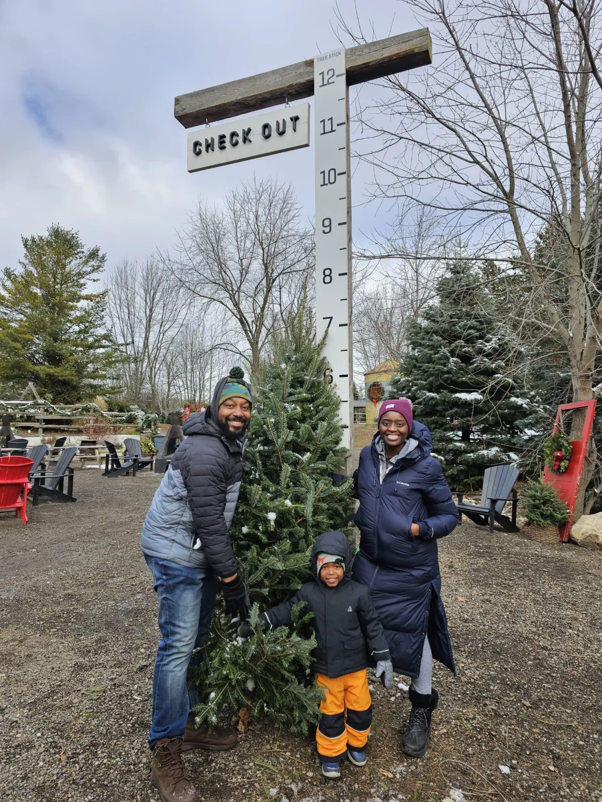 Family posing with a Christmas tree beside a height measurement scale outdoors.