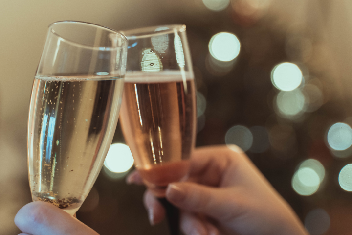 Two hands clinking champagne glasses with blurred lights in the background.