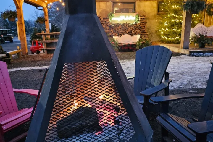 Outdoor fireplace surrounded by chairs, lit with string lights, near a decorated building.