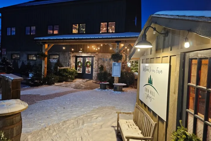 Snowy entrance to cabin-style shop with festive wreaths and warm lights at dusk.
