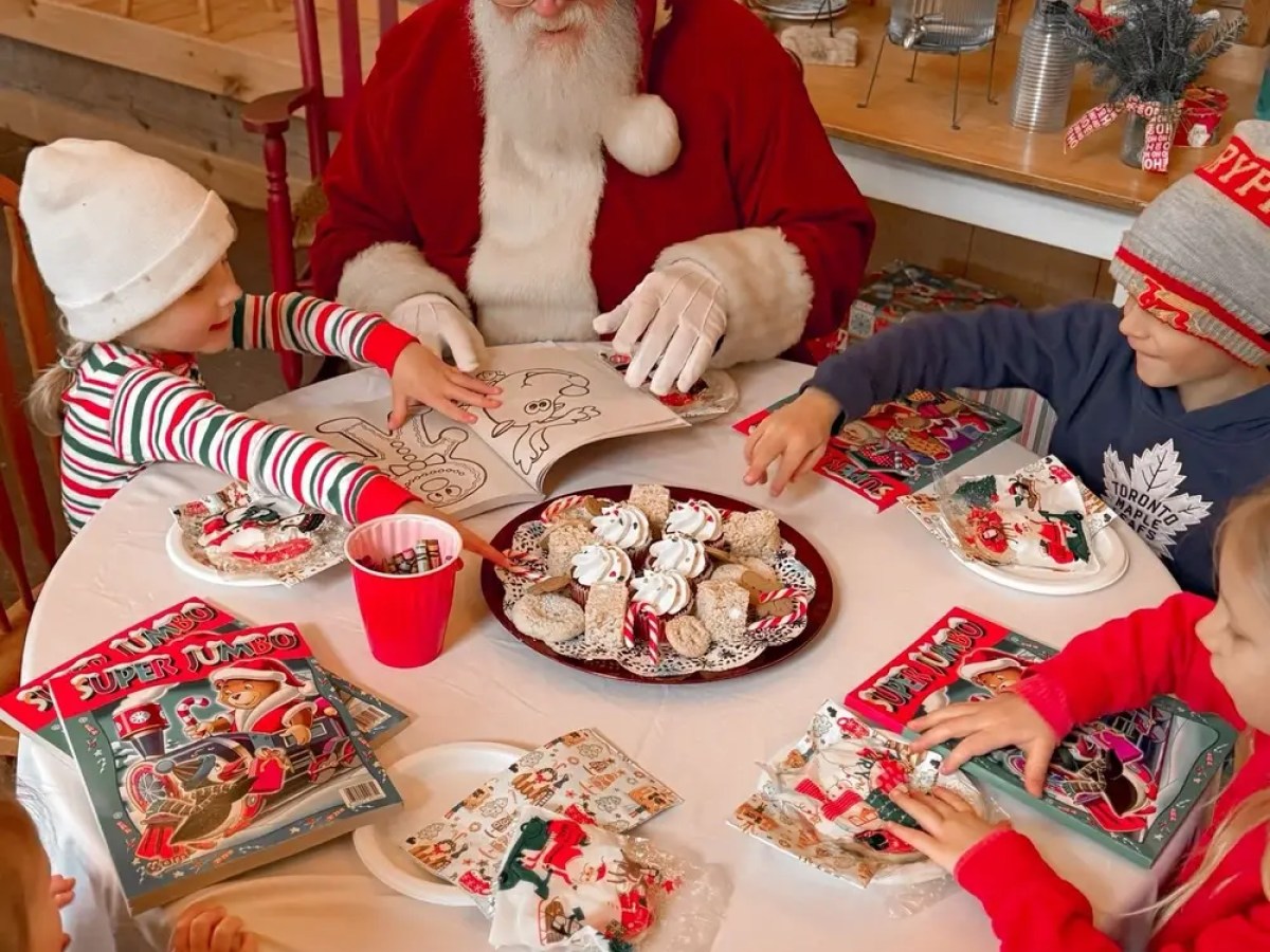 Santa and kids coloring at a table with Christmas treats.
