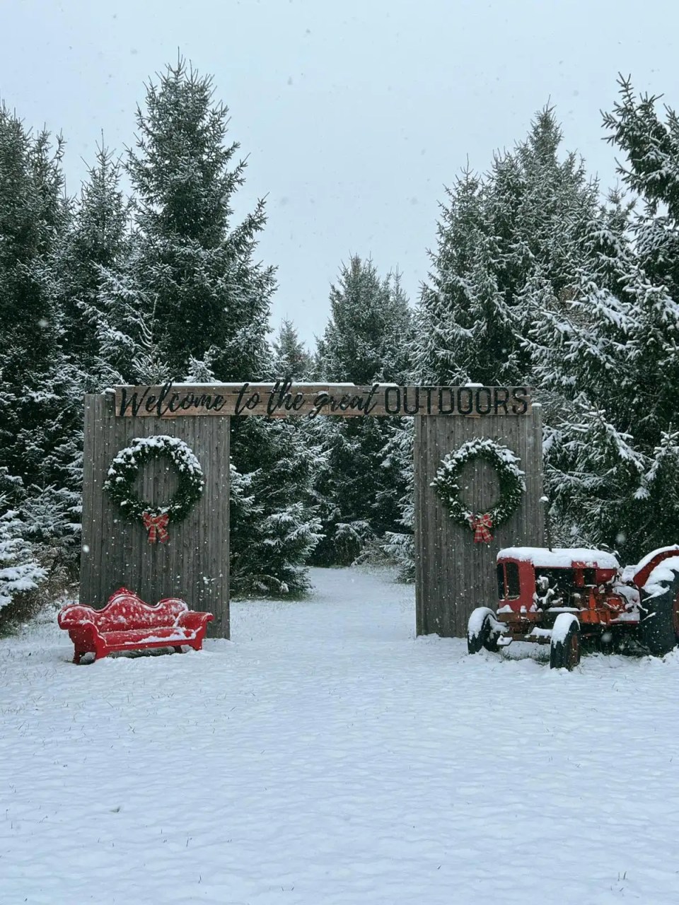 Snowy scene with trees, wooden archway, red bench, and tractor.