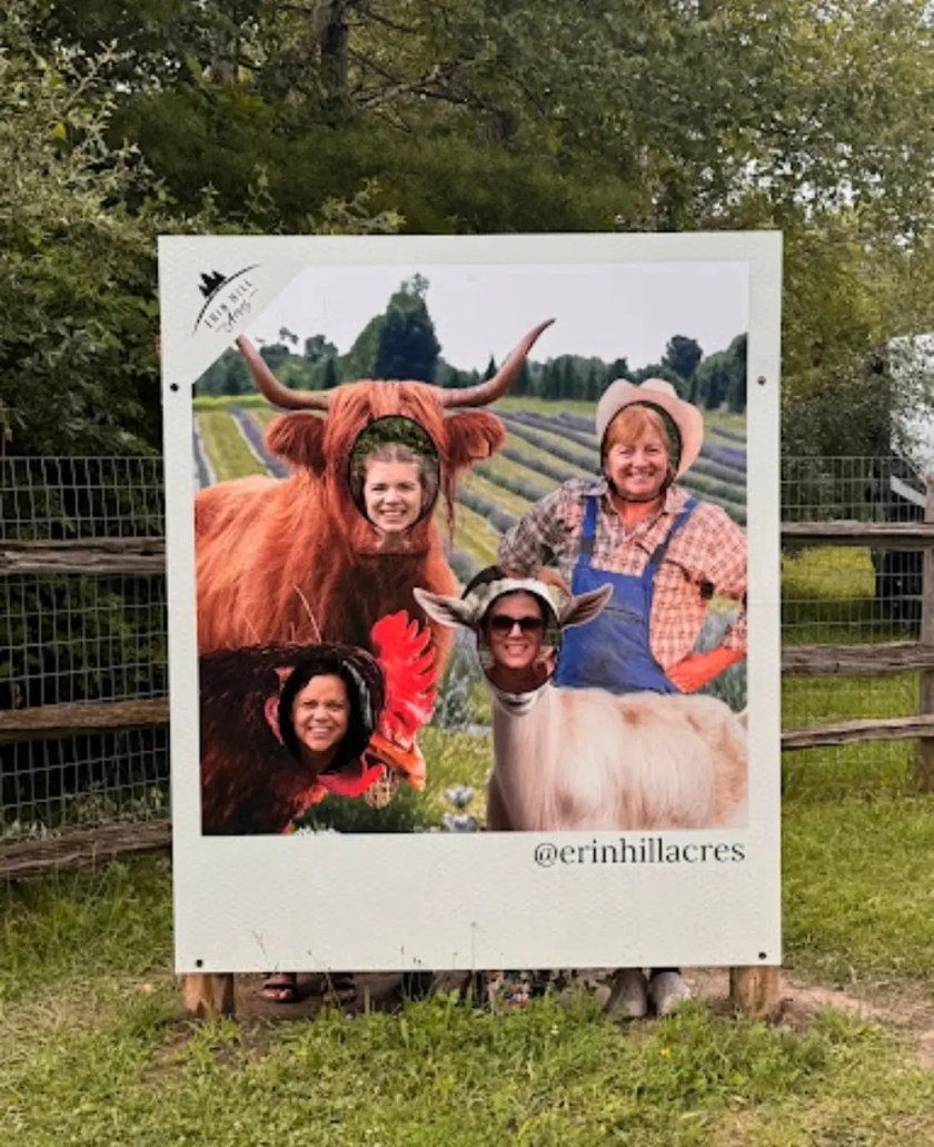 Four people pose behind animal cutouts on a sign at a farm.